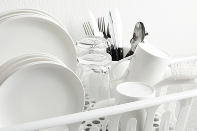 Photo of Drying rack with clean dishes and cutlery near white wall