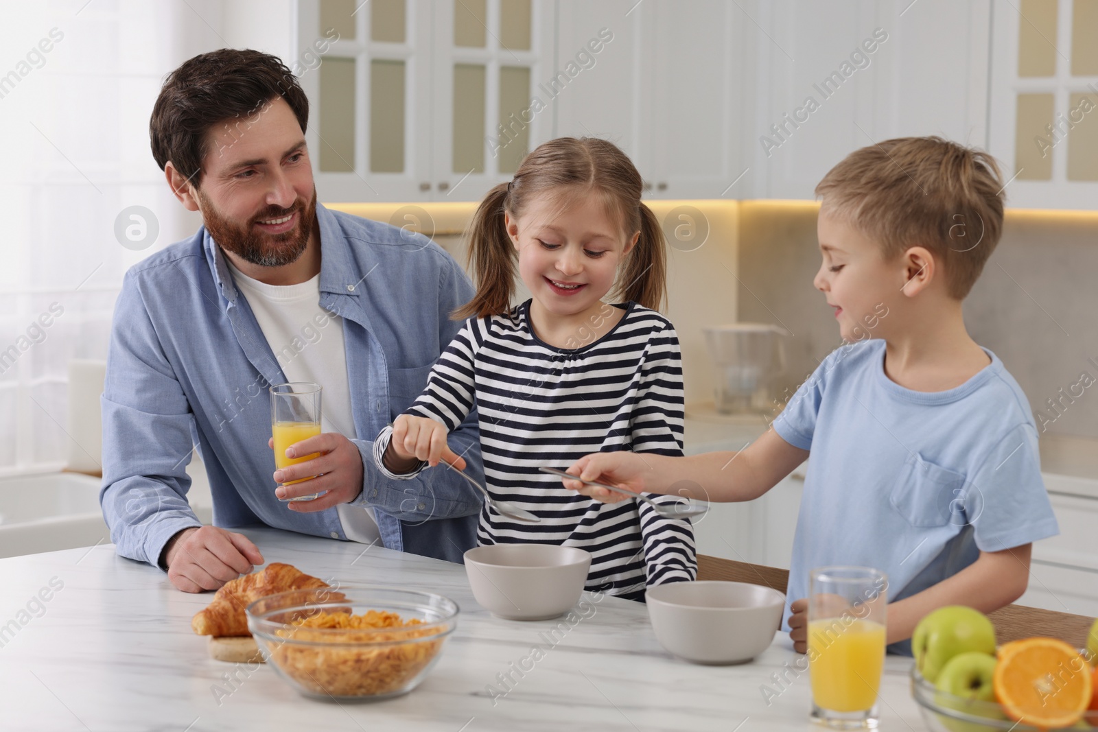Photo of Father and his little children having breakfast at table in kitchen