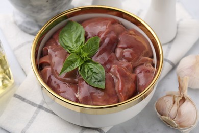 Photo of Bowl with raw chicken liver and basil on white marble table, closeup
