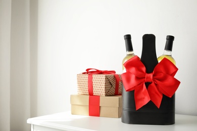 Photo of Bottles of wine in holder with bow and gift boxes on table in light room. Space for text