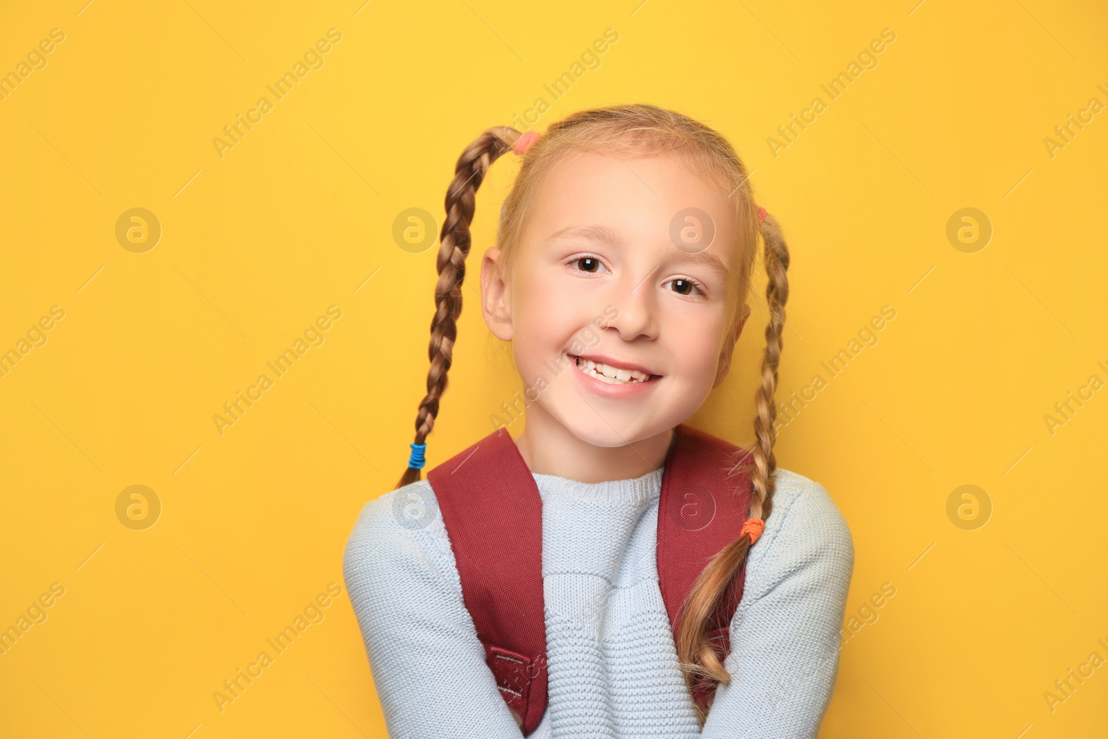 Photo of Cute little girl with backpack on yellow background