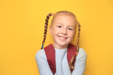 Photo of Cute little girl with backpack on yellow background