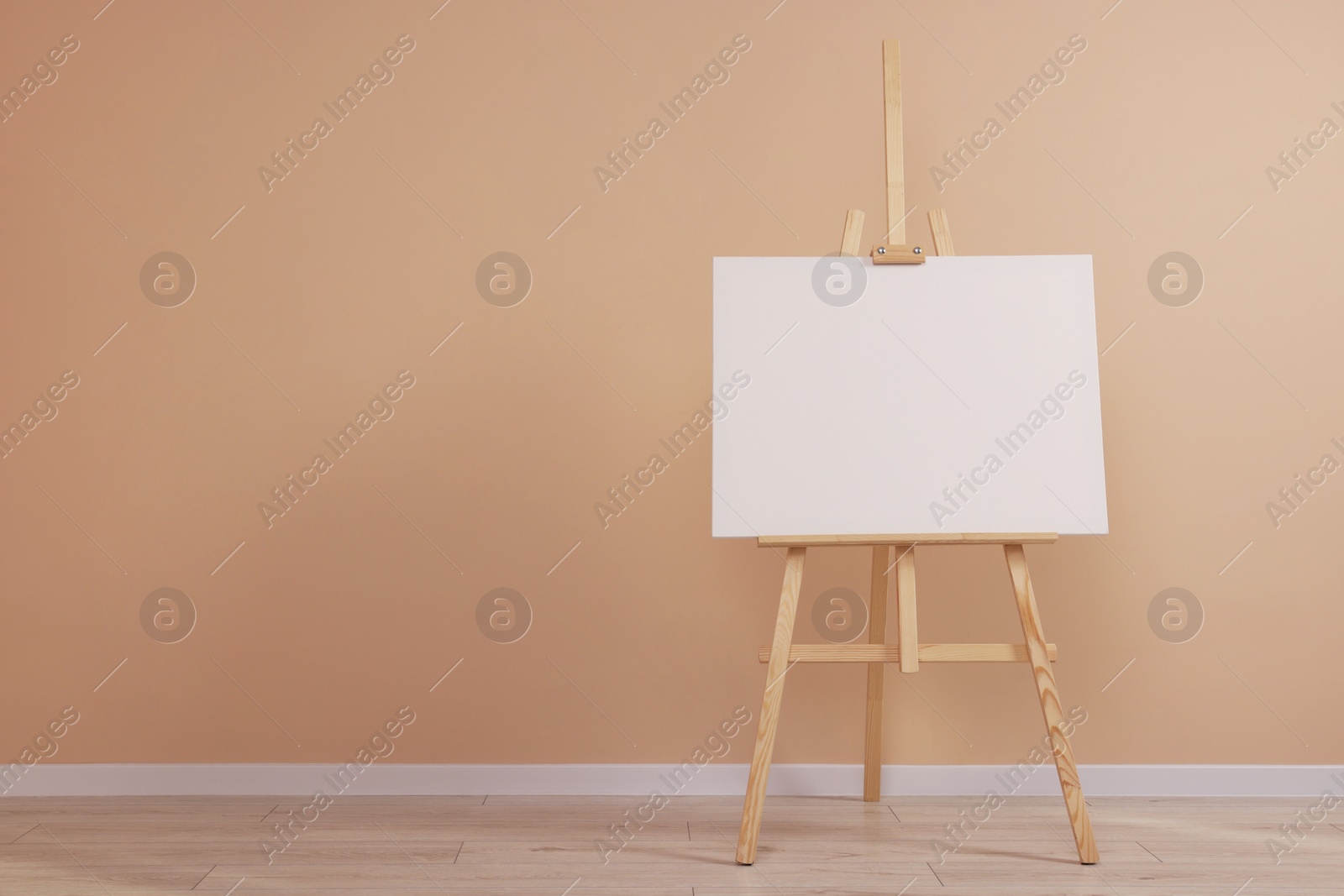 Photo of Wooden easel with blank canvas near beige wall indoors. Space for text