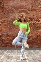 Photo of Beautiful young woman dancing hip hop near brick wall outdoors
