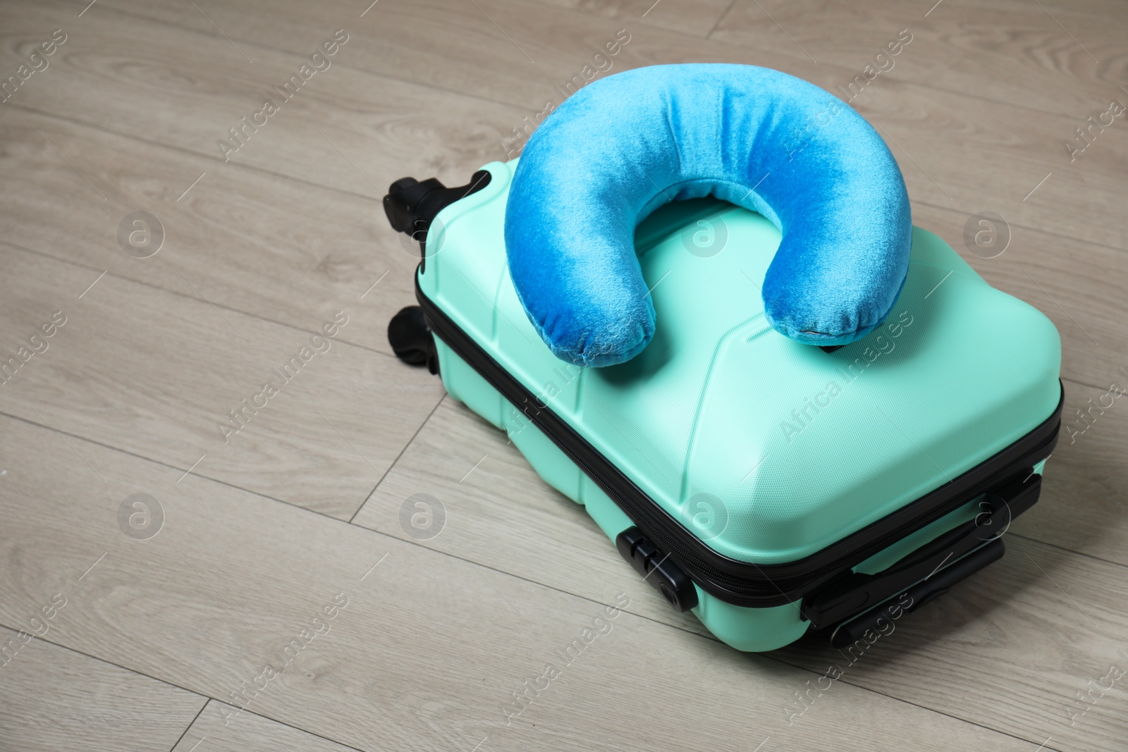 Photo of Turquoise travel pillow and suitcase on floor, space for text