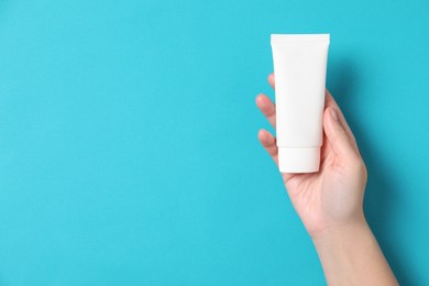 Woman with tube of hand cream on light blue background, top view. Space for text