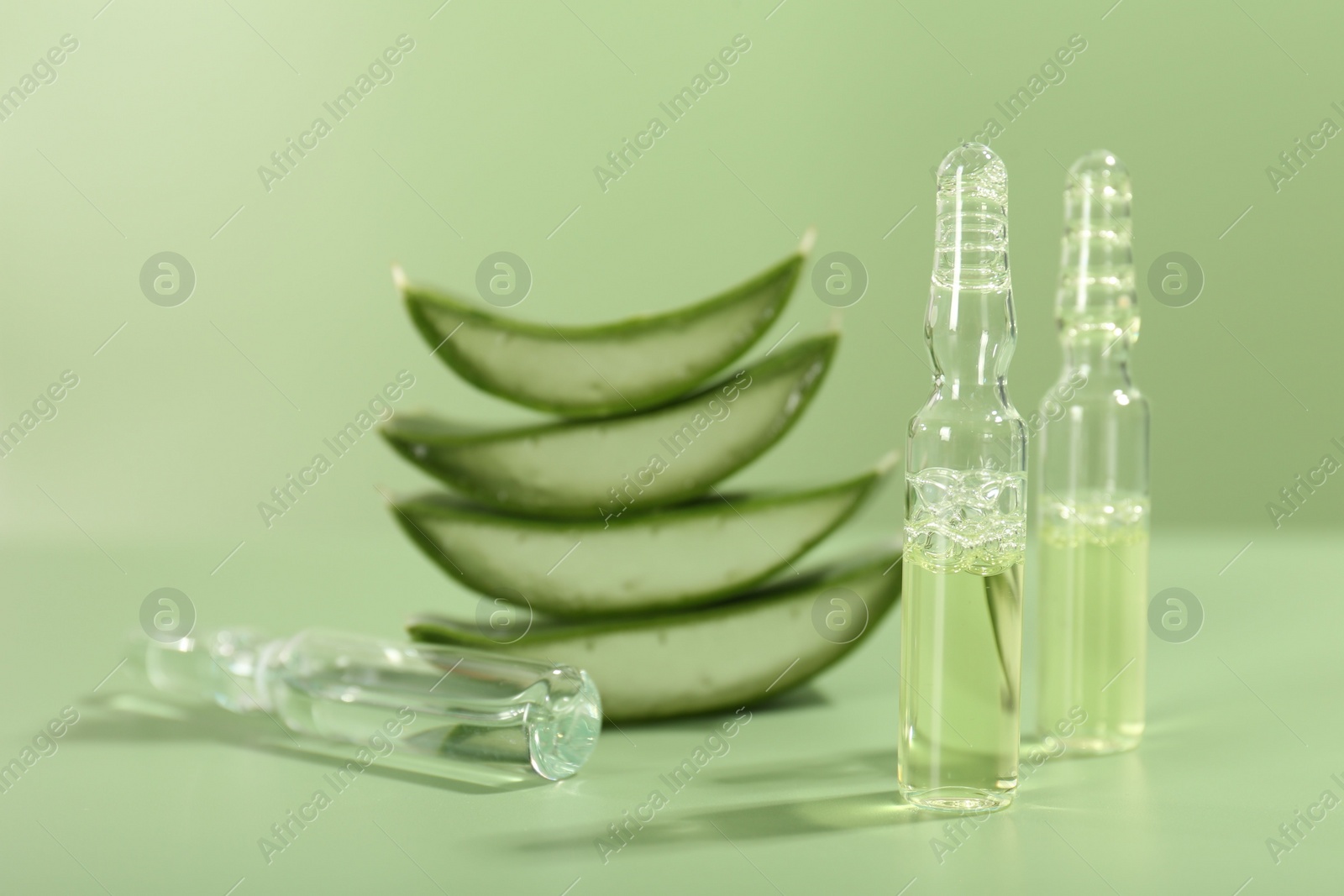 Photo of Skincare ampoules with extract of aloe vera and cut leaves on pale green background, closeup