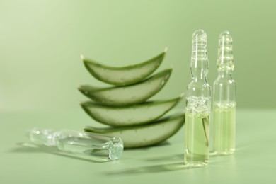 Skincare ampoules with extract of aloe vera and cut leaves on pale green background, closeup