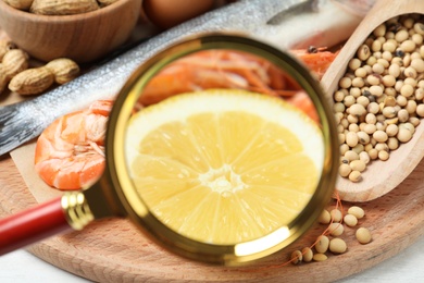 Photo of Different products with magnifier focused on lemon and shrimps, closeup. Food allergy concept