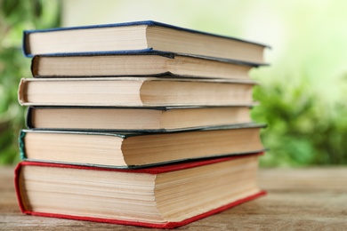 Stack of hardcover books on wooden table against blurred background