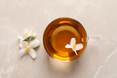 Photo of Glass cup of aromatic jasmine tea and fresh flowers on grey table, flat lay