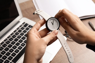 Woman winding up her wrist watch at office table, closeup. Time management