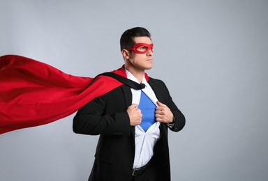 Photo of Businessman in superhero cape and mask taking suit off on grey background