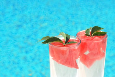 Photo of Refreshing watermelon drink in glasses near swimming pool outdoors, closeup. Space for text