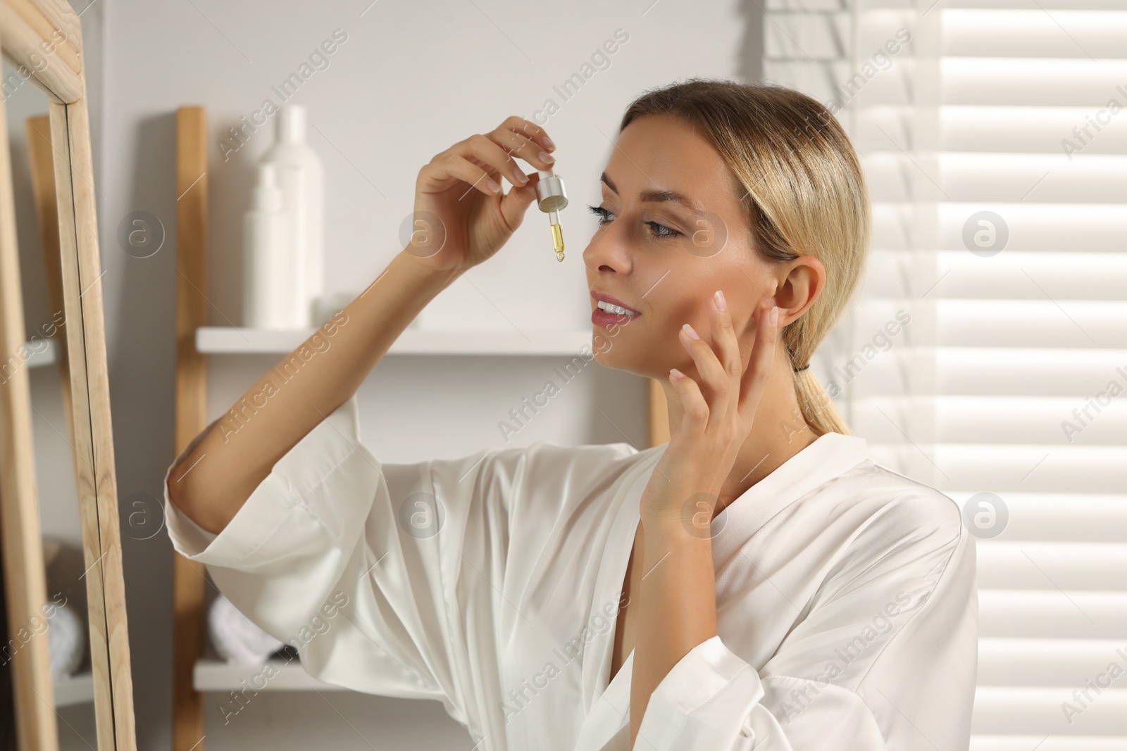 Photo of Beautiful woman applying cosmetic serum onto her face in bathroom