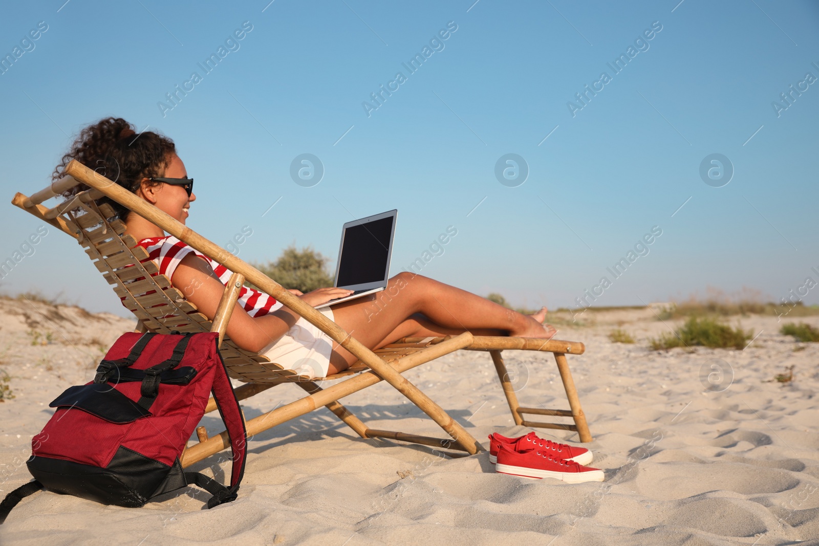 Photo of African American woman working on laptop in sunbed at beach