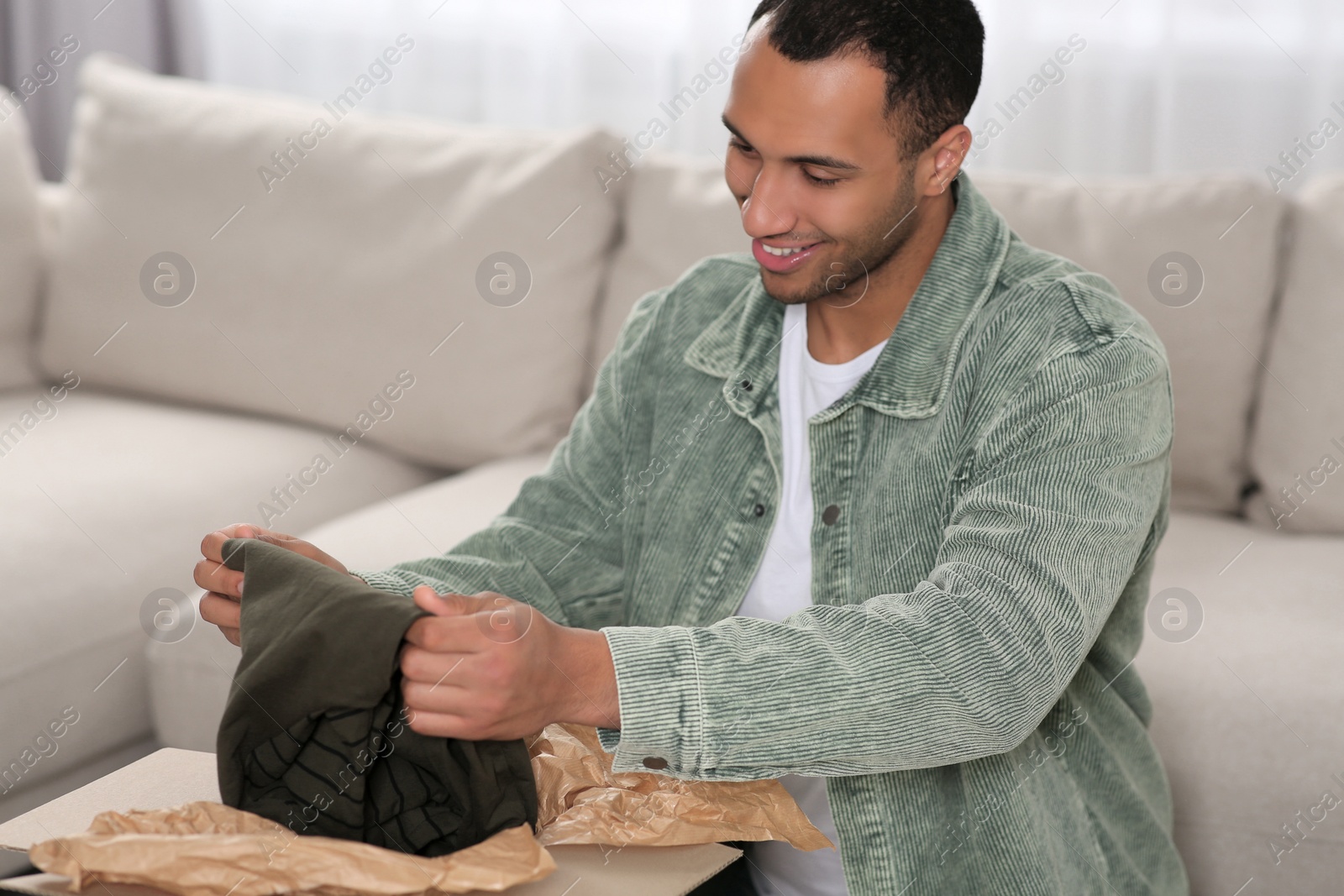 Photo of Happy young man opening parcel at home. Internet shopping