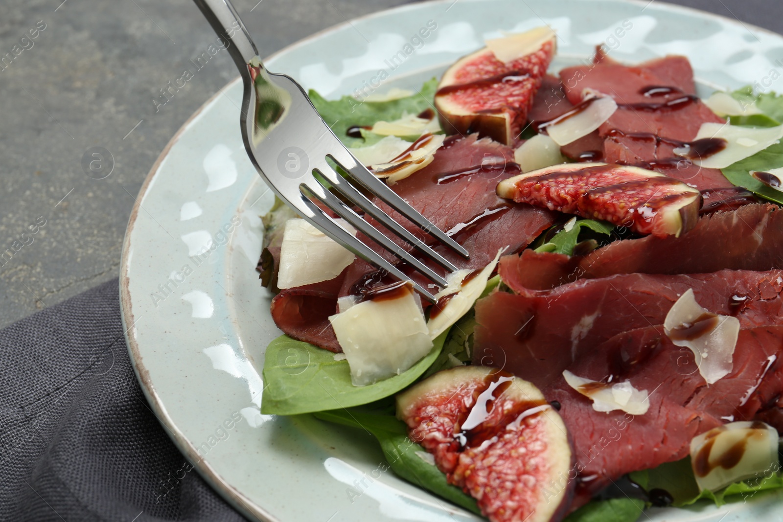 Photo of Eating delicious bresaola salad at grey table, closeup