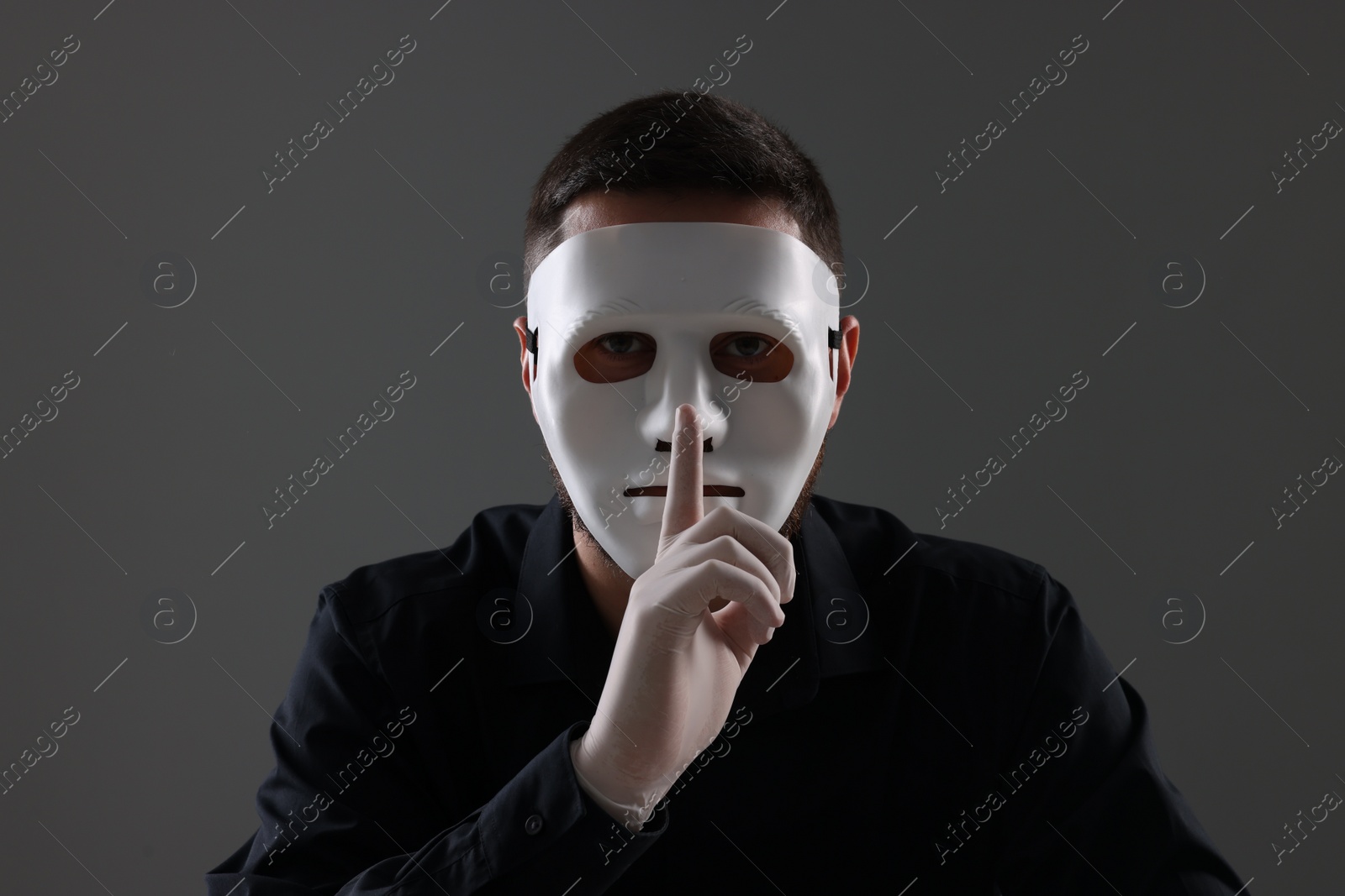 Photo of Man in mask and gloves showing hush gesture against grey background