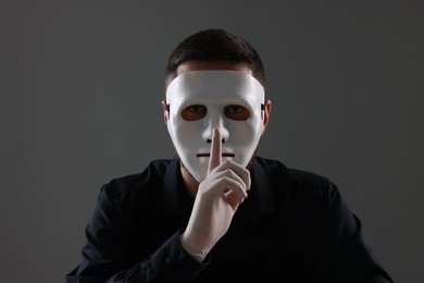 Man in mask and gloves showing hush gesture against grey background