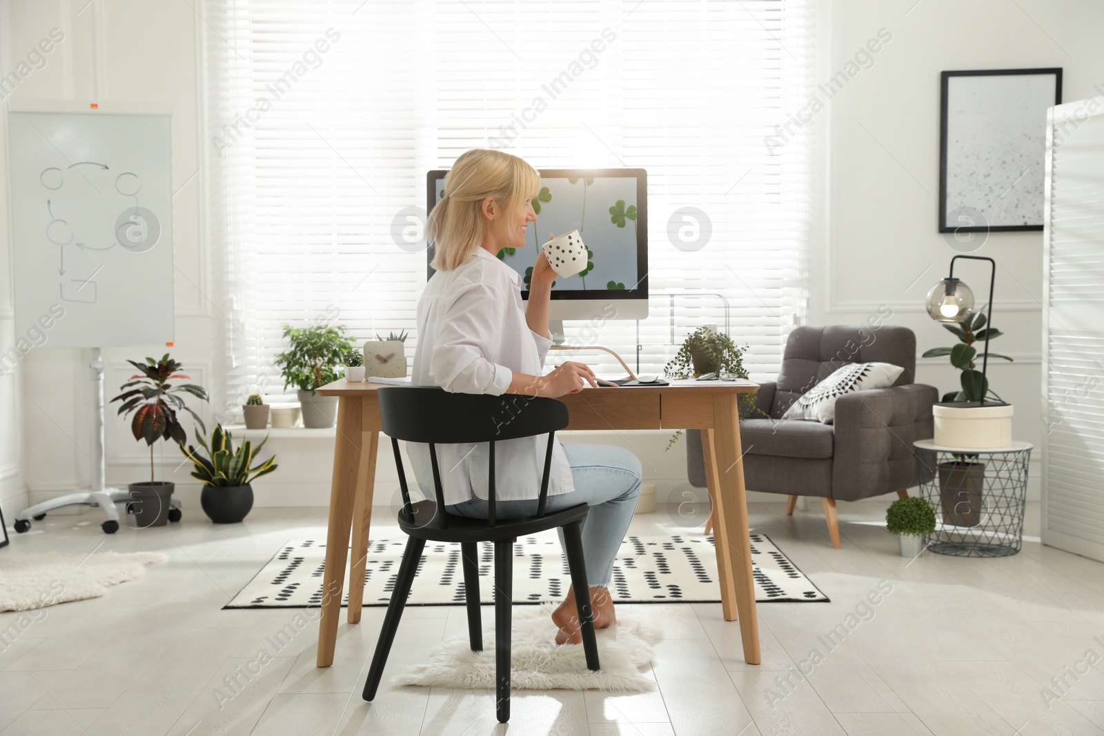 Photo of Woman with cup of tea at table in light room. Home office