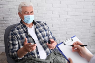 Doctor examining senior man in protective mask at nursing home