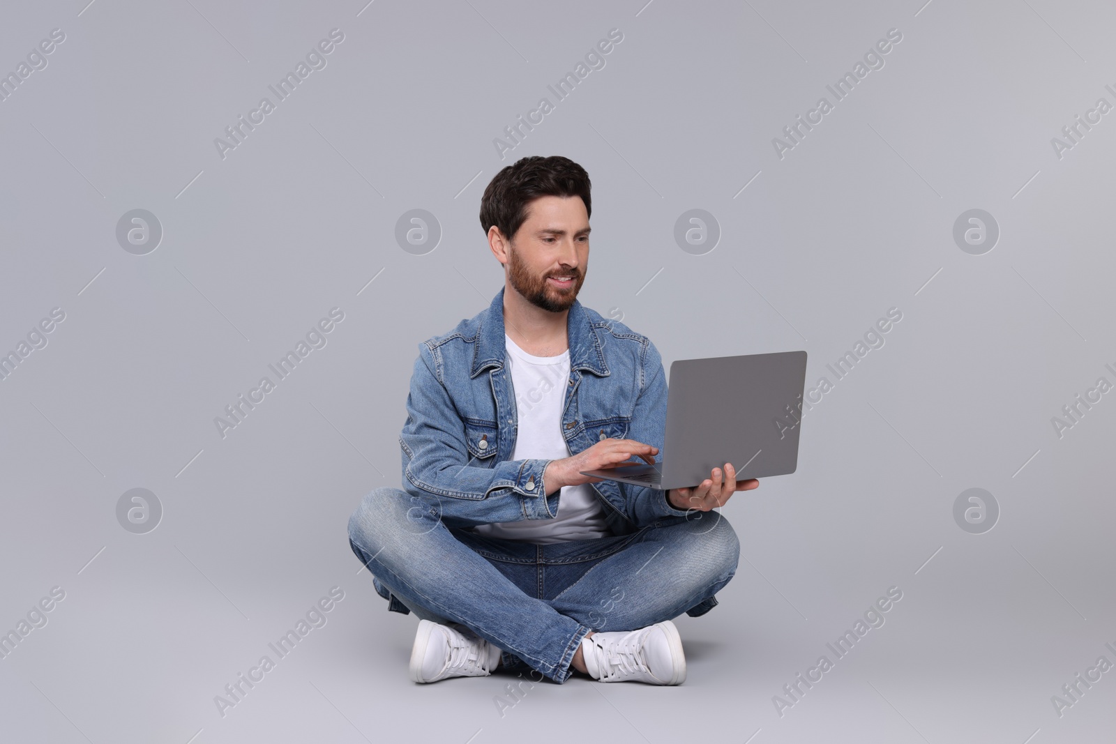 Photo of Happy man with laptop on light grey background