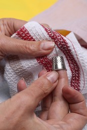 Photo of Woman embroidering on fabric with thimble and sewing needle against yellow background, closeup