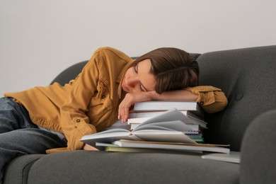Young tired woman sleeping near books on couch indoors