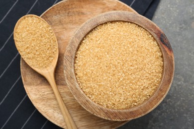 Brown sugar in bowl and spoon on grey table, top view