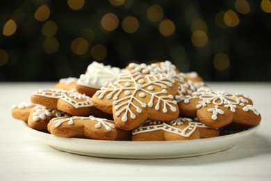 Tasty Christmas cookies with icing on white wooden table against blurred lights, closeup