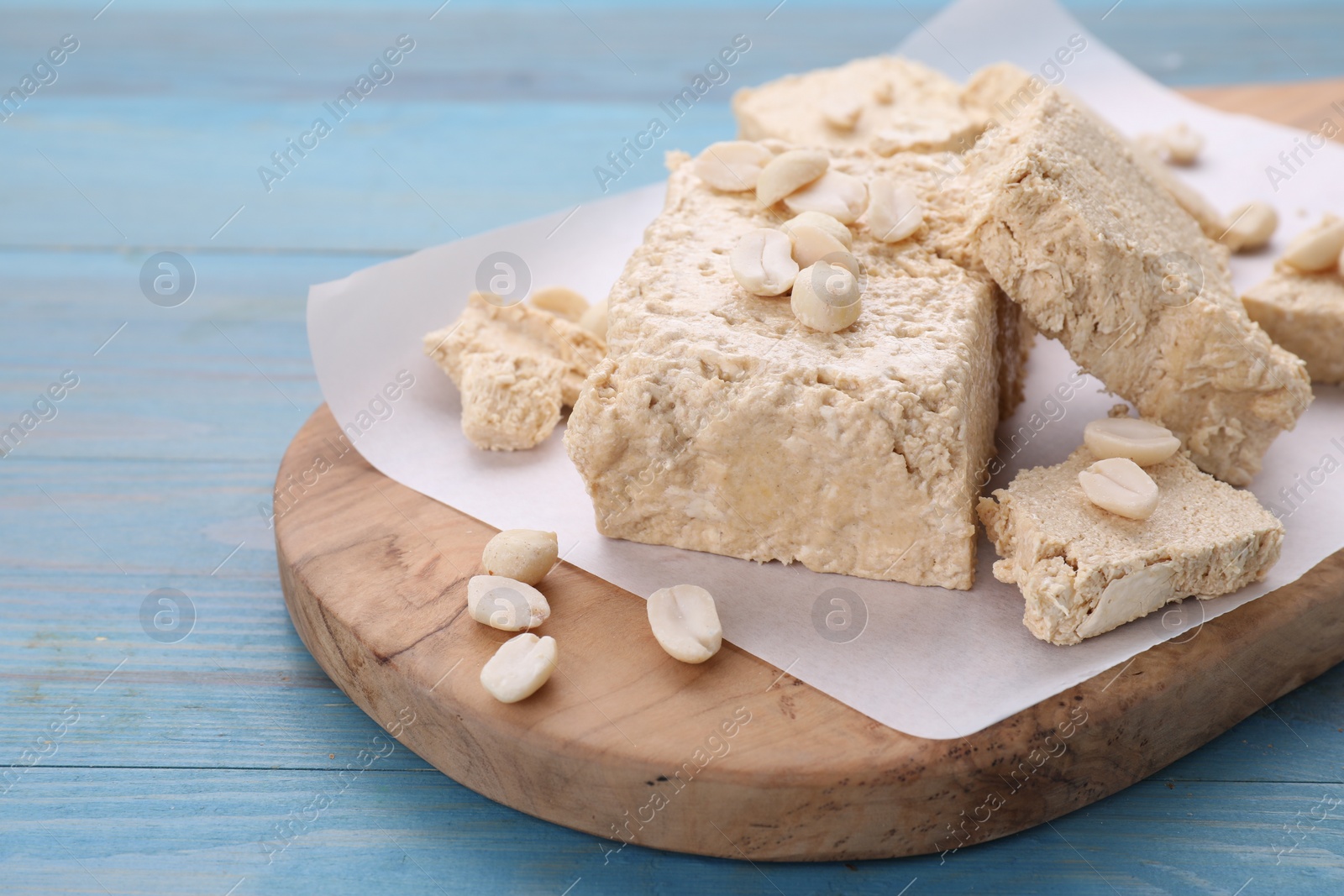 Photo of Pieces of tasty halva and peanuts on light blue wooden table, closeup. Space for text