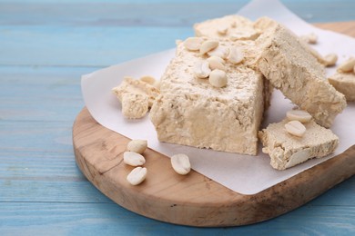 Pieces of tasty halva and peanuts on light blue wooden table, closeup. Space for text