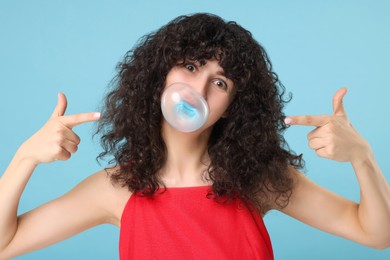 Beautiful young woman blowing bubble gum on light blue background