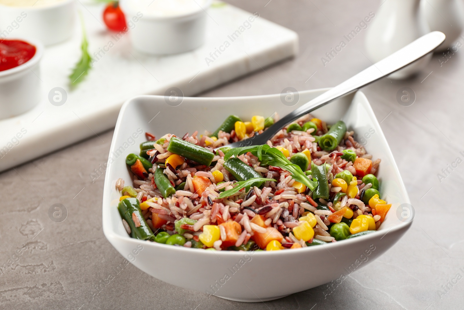 Photo of Tasty brown rice with vegetables on grey table