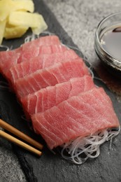 Photo of Tasty sashimi (pieces of fresh raw tuna), glass noodles and chopsticks on black board, closeup