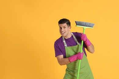 Photo of Emotional man with green broom on orange background, space for text
