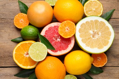 Different ripe citrus fruits with green leaves on wooden table, flat lay