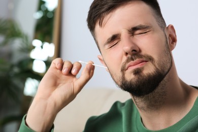 Photo of Young man cleaning ear with cotton swab at home