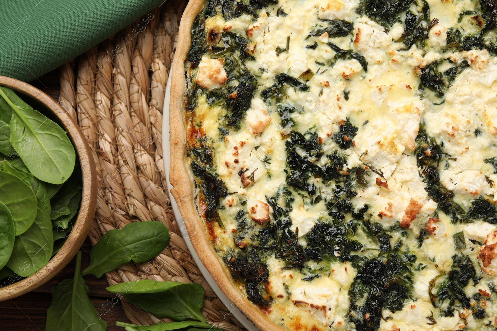 Photo of Delicious homemade quiche and spinach leaves on wicker mat, flat lay