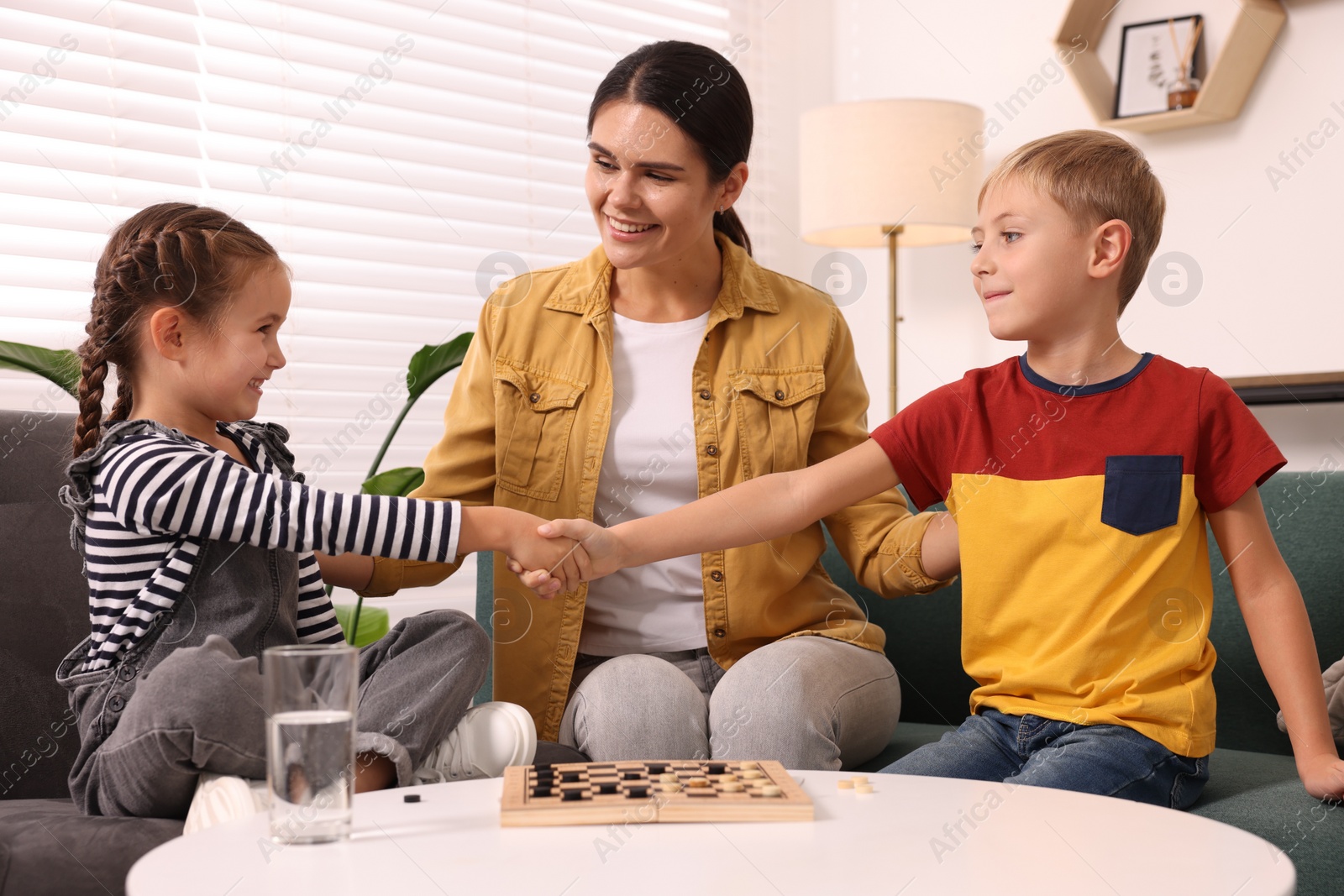 Photo of Family playing checkers at coffee table in room. Children shaking hands after game