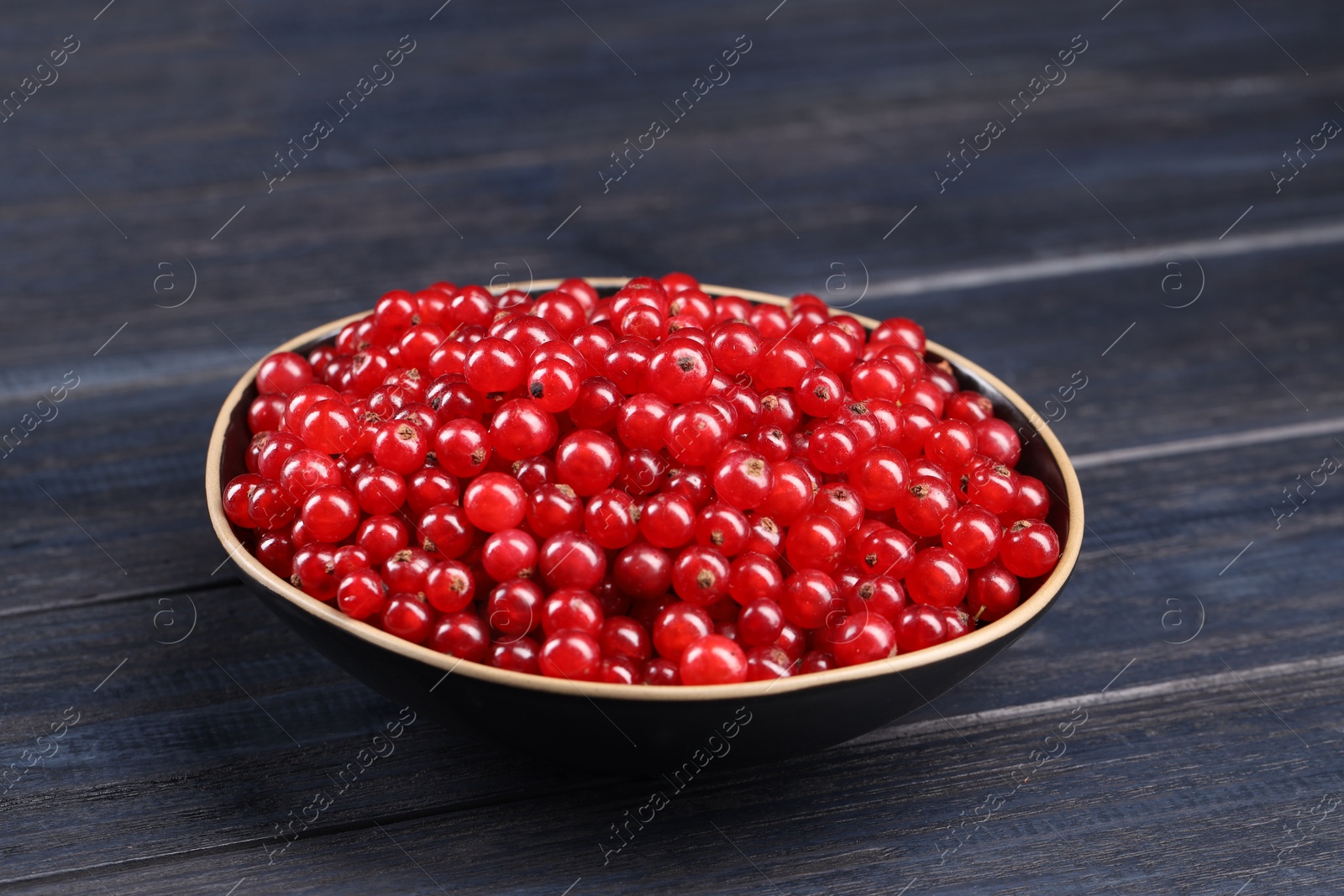 Photo of Ripe red currants in bowl on wooden rustic table