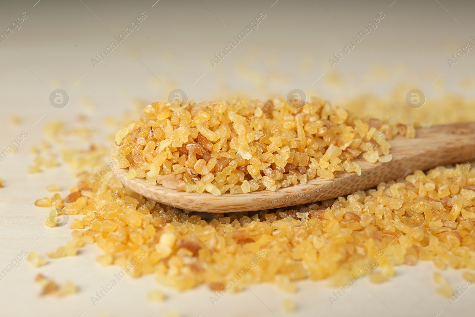 Photo of Spoon with uncooked bulgur on wooden table, closeup