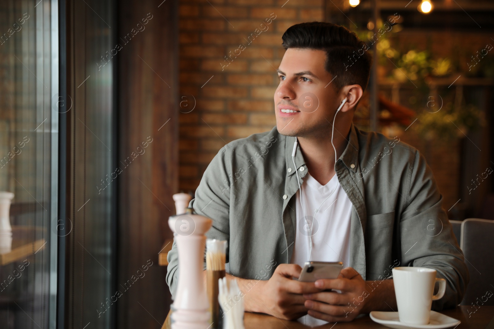 Photo of Man with smartphone listening to audiobook at table in cafe