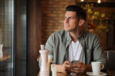 Photo of Man with smartphone listening to audiobook at table in cafe