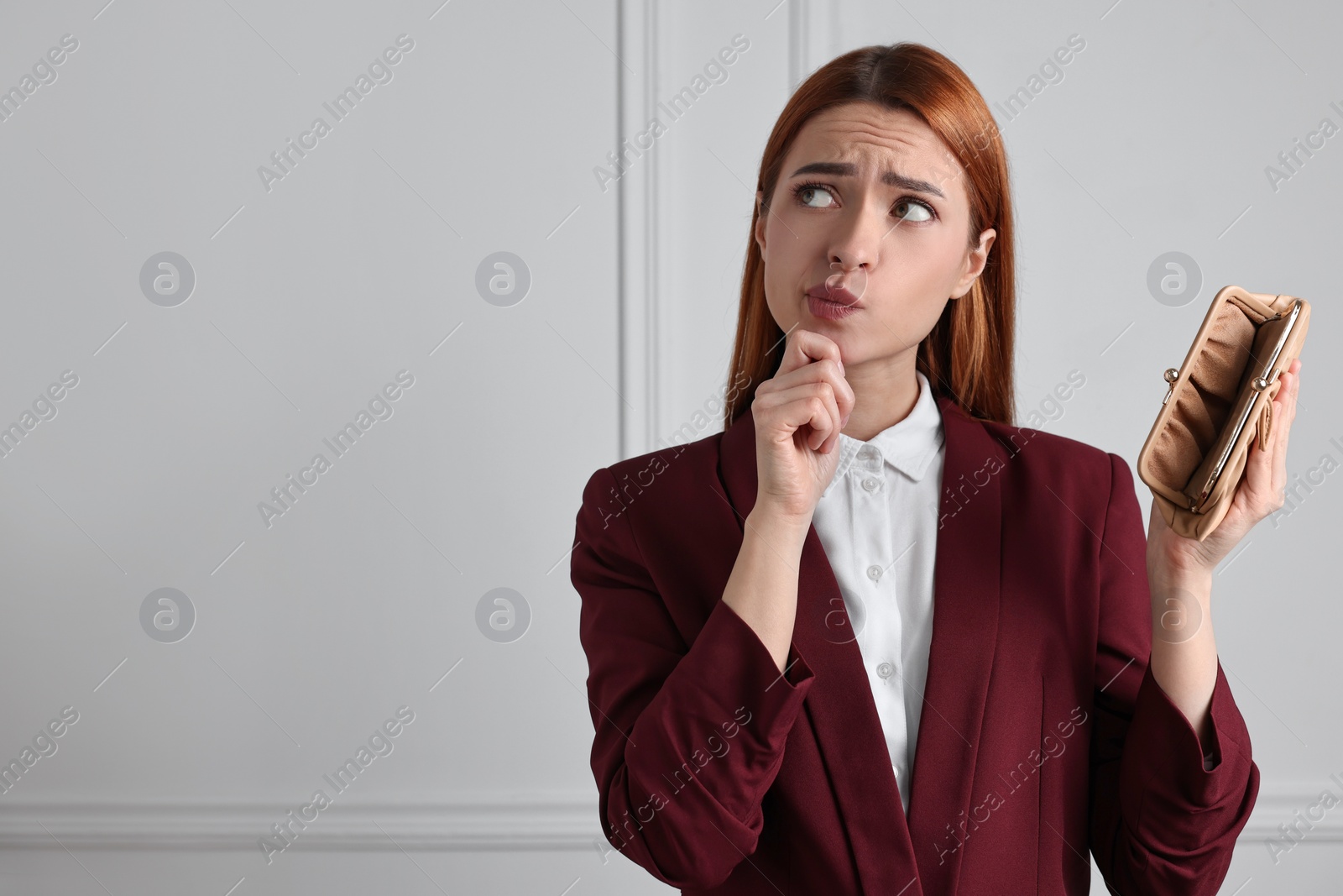 Photo of Confused woman with empty wallet near white wall, space for text