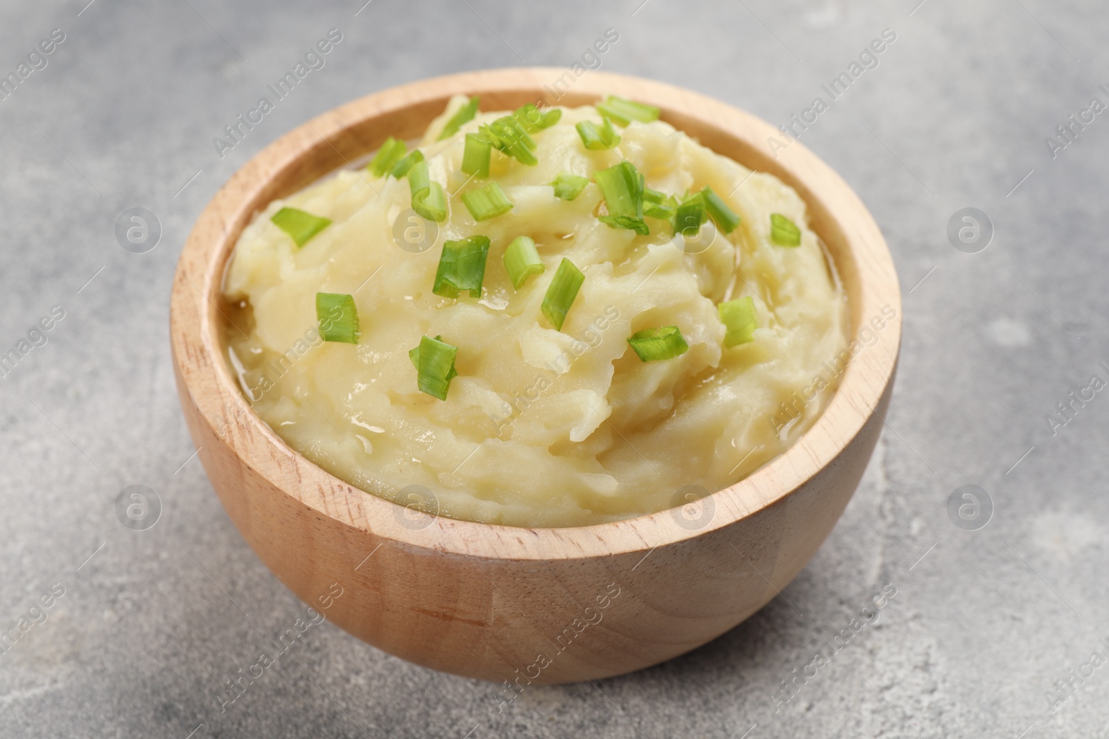 Photo of Bowl of tasty mashed potato with greens on grey marble table, closeup