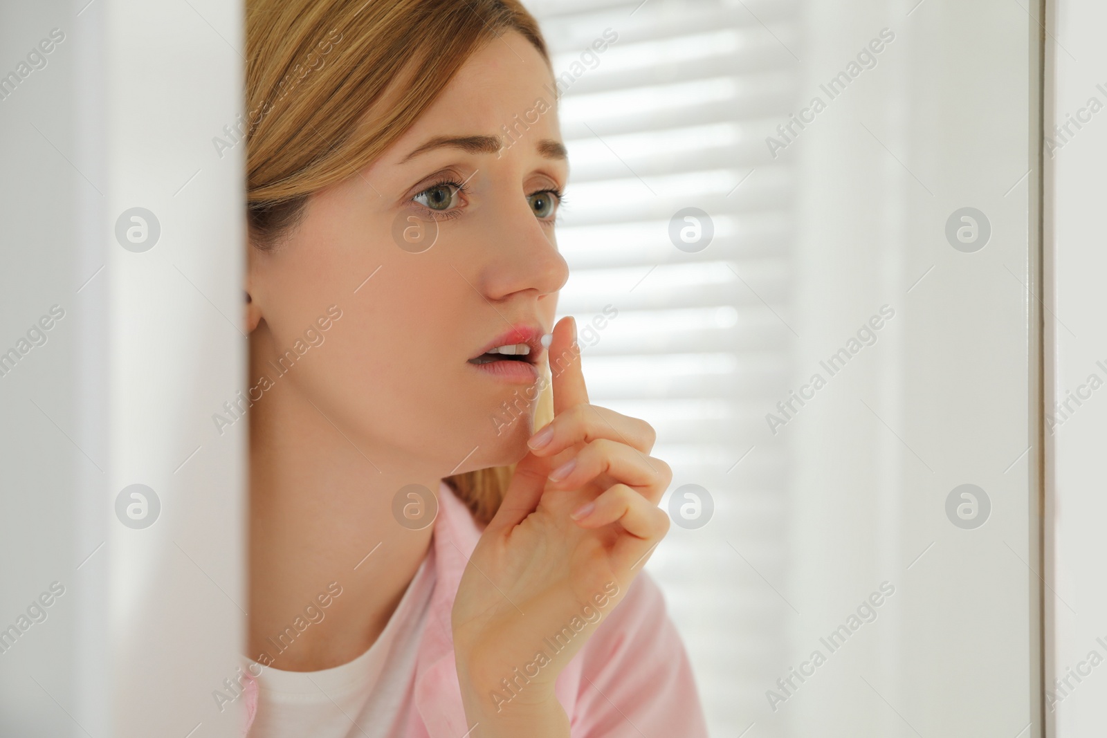 Photo of Woman with herpes applying cream on lips near mirror indoors