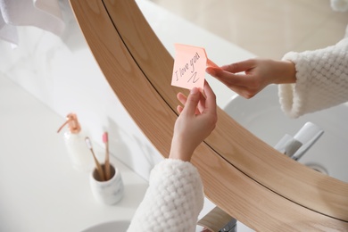 Woman with sticky note saying I Love You near mirror in bathroom, closeup. Romantic message