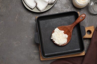 Baking dish with coconut oil and wooden spoon on grey table, flat lay. Space for text